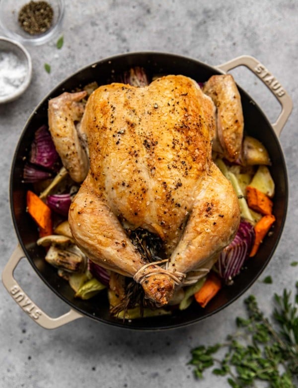 full roasted chicken in a dutch oven surrounded by roasted vegetables