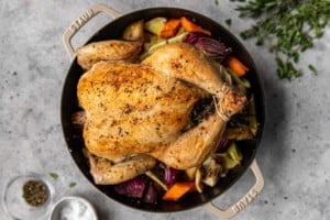 full roasted chicken surrounded by vegetables in a black dutch oven pot