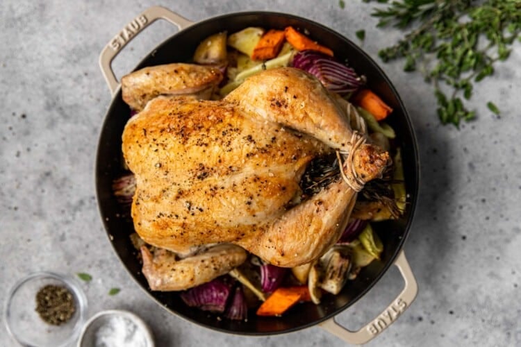 full roasted chicken surrounded by vegetables in a black dutch oven pot
