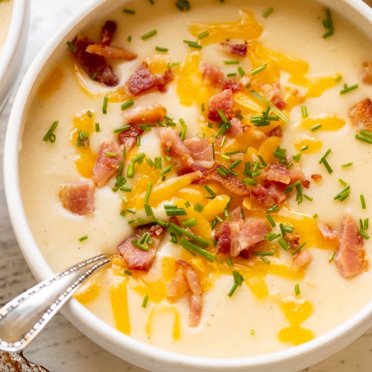 baked potato soup in a white bowl garnished with bacon, cheese and chives.