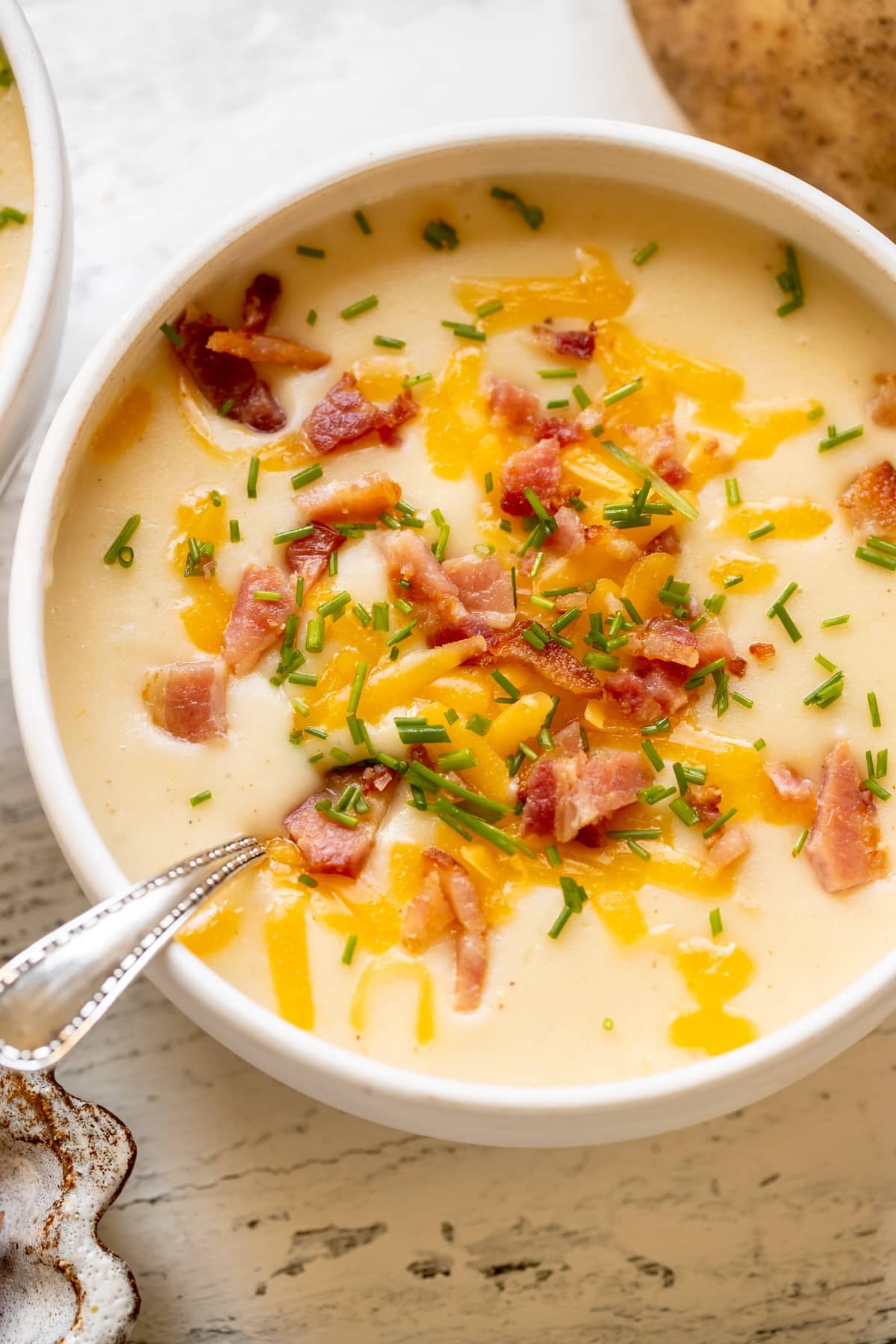 baked potato soup in a white bowl garnished with bacon, cheese and chives.