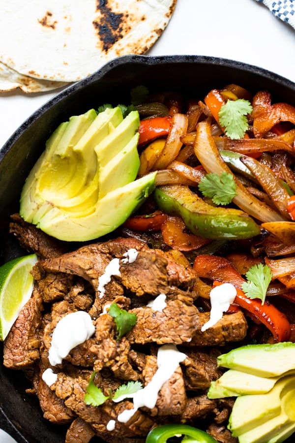 flank steak and bell peppers and onions in a cast iron skillet for flank steak fajitas