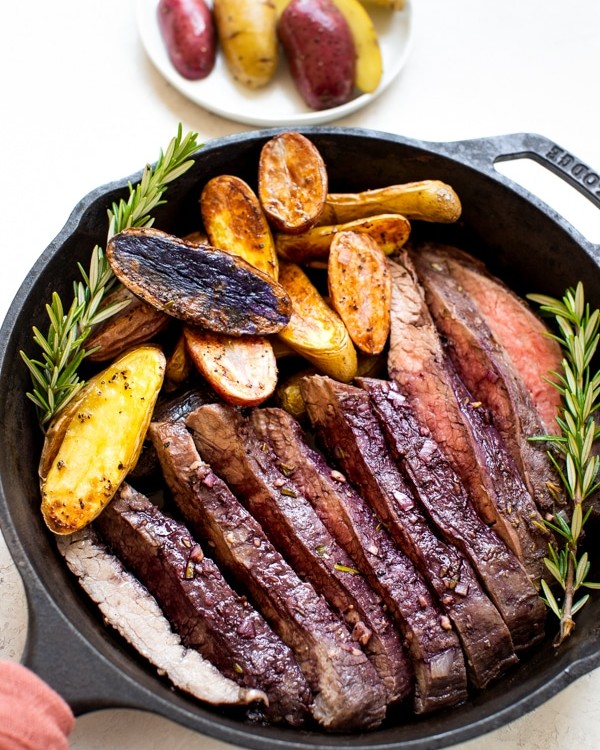 baked flank steak and fingerling potatoes in a cast iron skillet