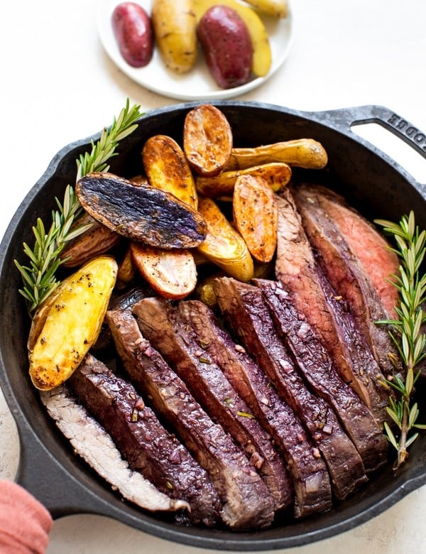 baked flank steak and fingerling potatoes in a cast iron skillet