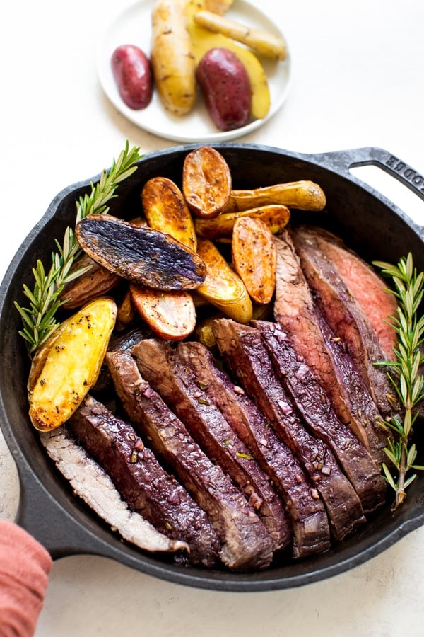 baked flank steak and fingerling potatoes in a cast iron skillet