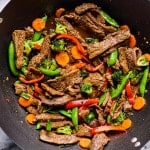 Overhead view of a wok filled with beef stir fry featuring seared beef strips, bright carrots, broccoli florets, snap peas, and red bell peppers in a glossy sauce.