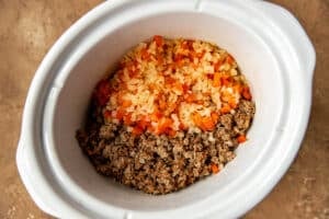 onions, peppers and meat in a white crock pot.
