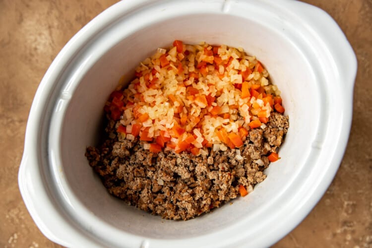 onions, peppers and meat in a white crock pot.