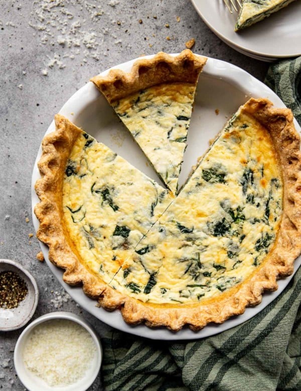 spinach quiche with two pieces missing in a white pie pan