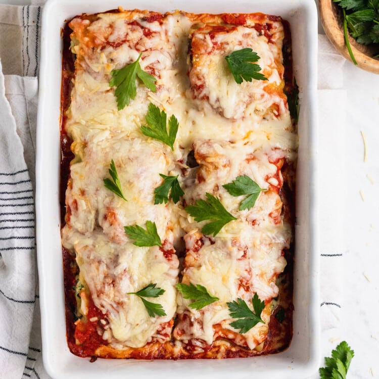 cheesy spinach ricotta rolled up into a lasagna noodle covered in red sauce in a casserole dish