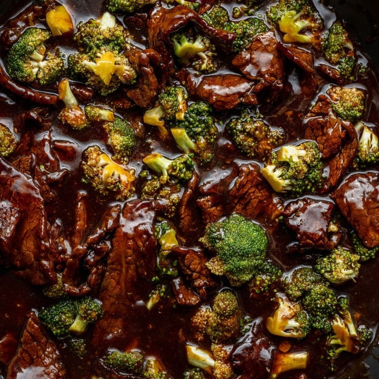 Close-up of beef and broccoli stir-fry in a dark sauce inside a skillet, showing tender beef slices and bright green broccoli coated in glossy sauce.