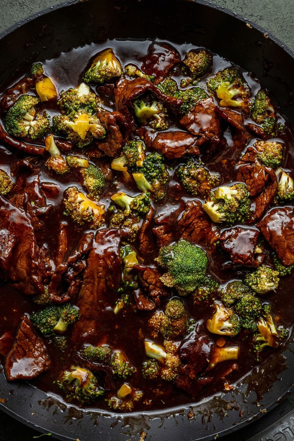 Close-up of beef and broccoli stir-fry in a dark sauce inside a skillet, showing tender beef slices and bright green broccoli coated in glossy sauce.