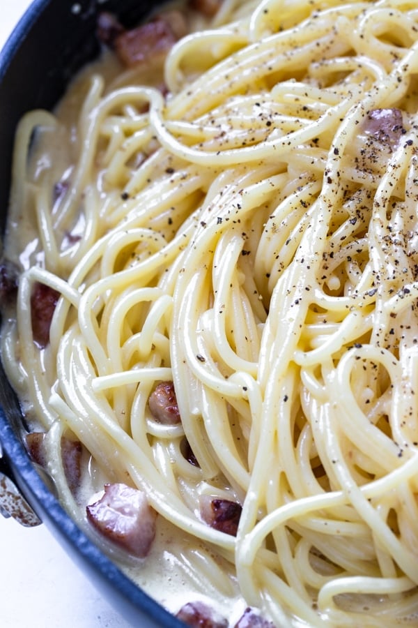 spaghetti carbonara in a non stick frying pan garnished with black pepper