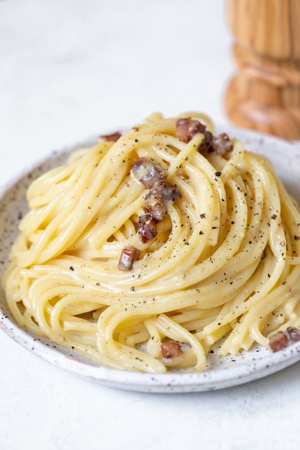 spaghetti carbonara on a speckled plate garnished with black pepper