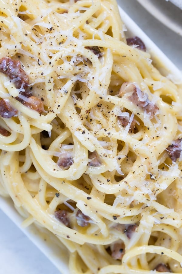 spaghetti carbonara on a white plate garnished with black pepper