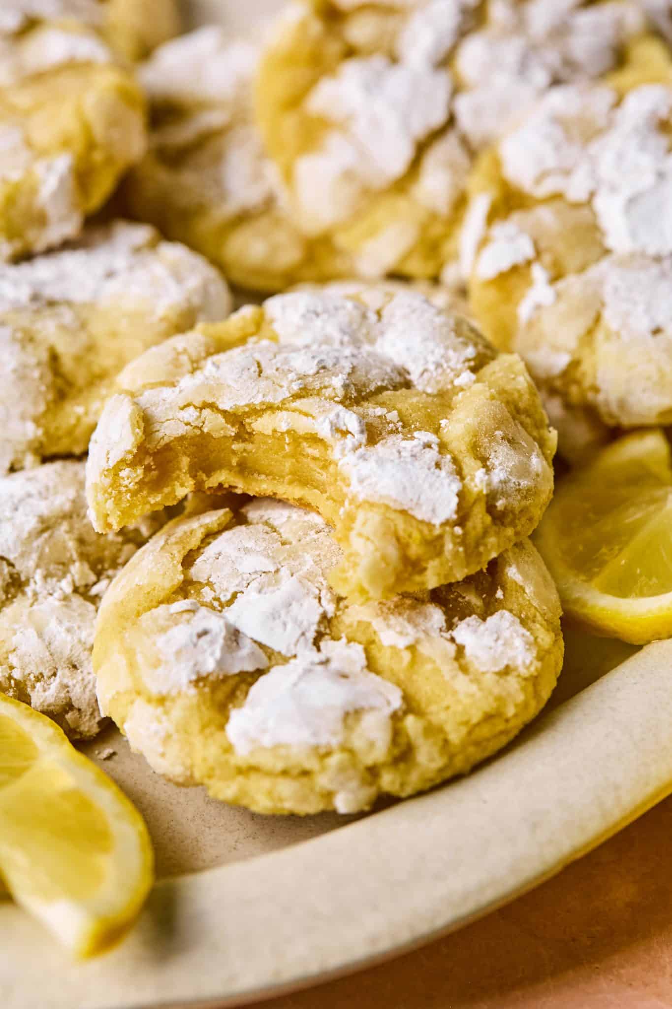 Close-up of a bitten lemon crinkle cookie stacked on top of others, showing a soft, moist interior and crackly sugar-dusted exterior.

