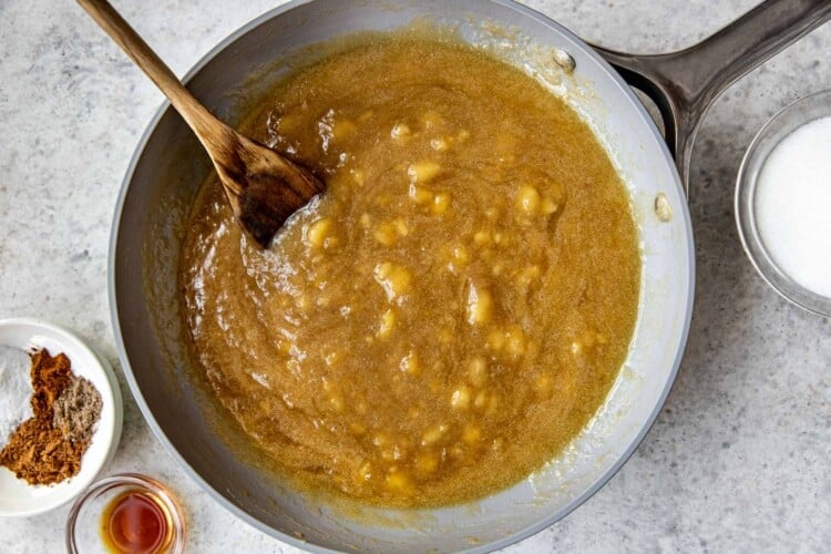 mashed bananas in a saute pan with a wooden spoon.