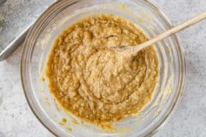 banana bread batter in a large glass bowl with a wooden spoon.