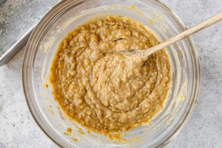 banana bread batter in a large glass bowl with a wooden spoon.