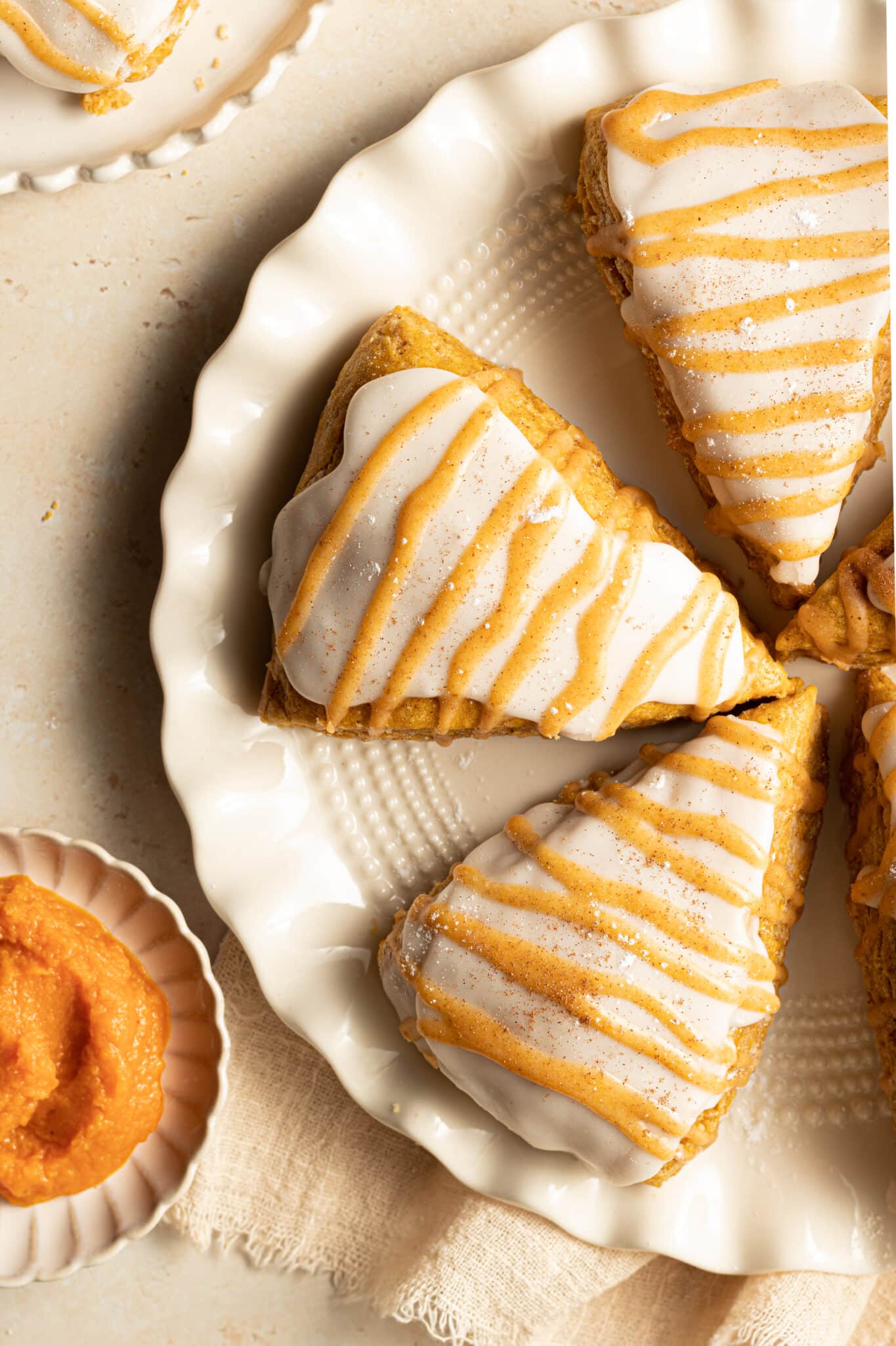 pumpkin scones on a white plate with glaze on top.