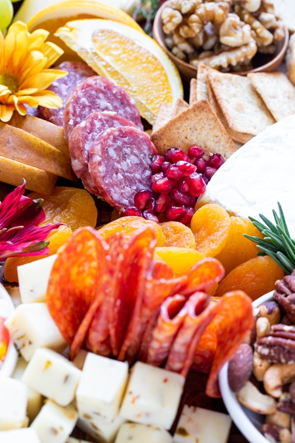 a charcuterie board filled with fruits, meats and cheese on a wood cutting board