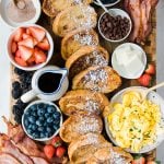 a cutting board filled with french toast, fresh berries, bacon and syrup