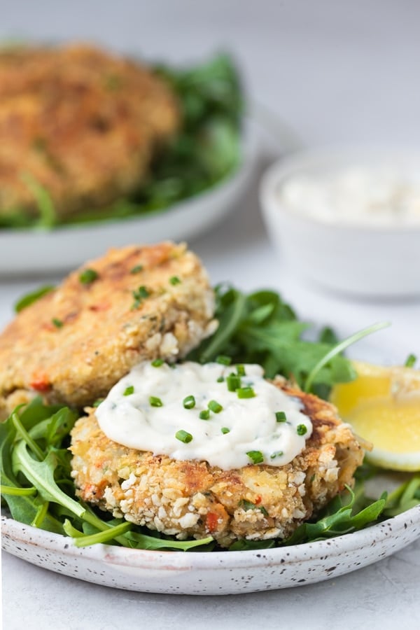 crab cakes on a plate with creamy special sauce on top garnished with chives 