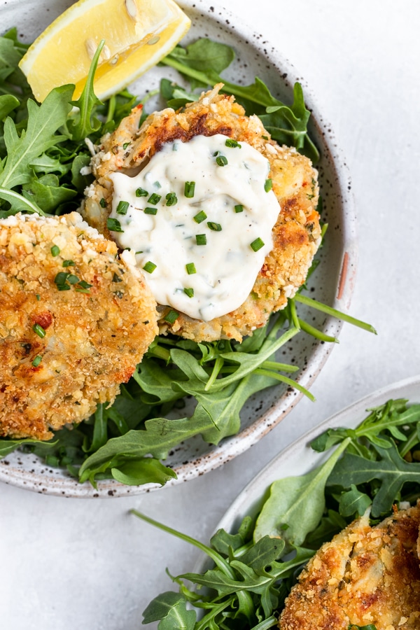 crab cakes on a plate with creamy special sauce on top garnished with chives 