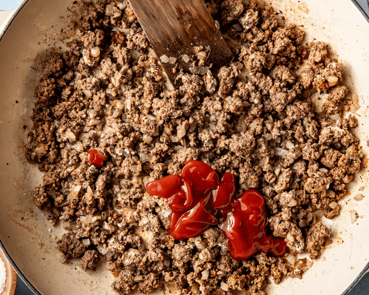 Adding ketchup and Worcestershire sauce to ground beef.