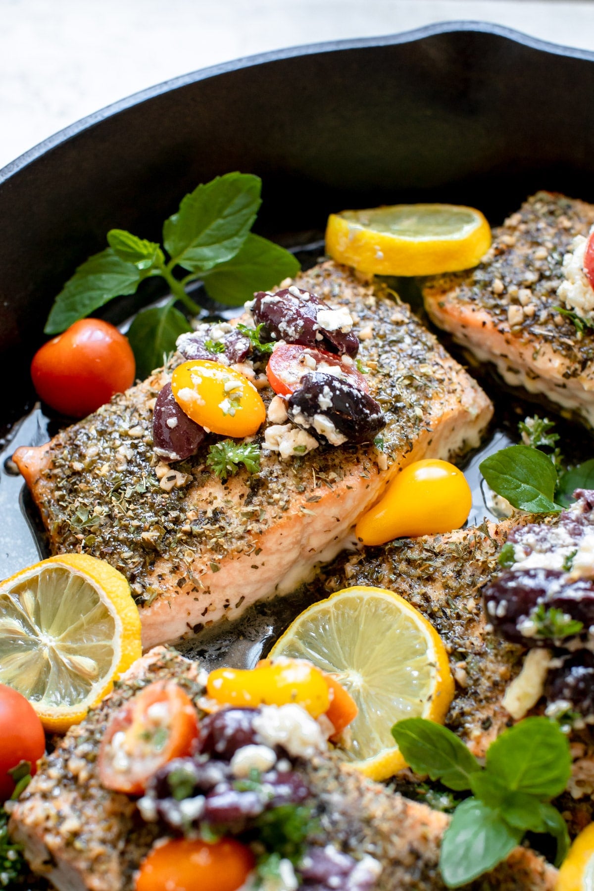 cooked mediterranean salmon with tomatoes and kalamata olives on top in a cast iron pan