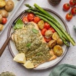 Sheet pan pesto salmon plated with roasted asparagus, crispy baby potatoes, blistered cherry tomatoes, fresh basil, grated Parmesan cheese, and lemon wedges.