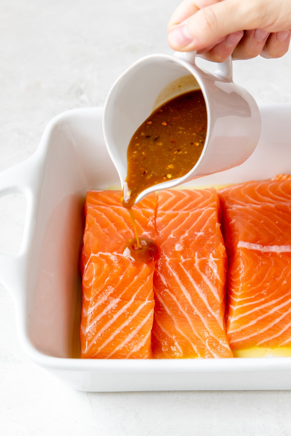 brown sugar miso sauce being poured onto fresh salmon fillets in a white baking dish 
