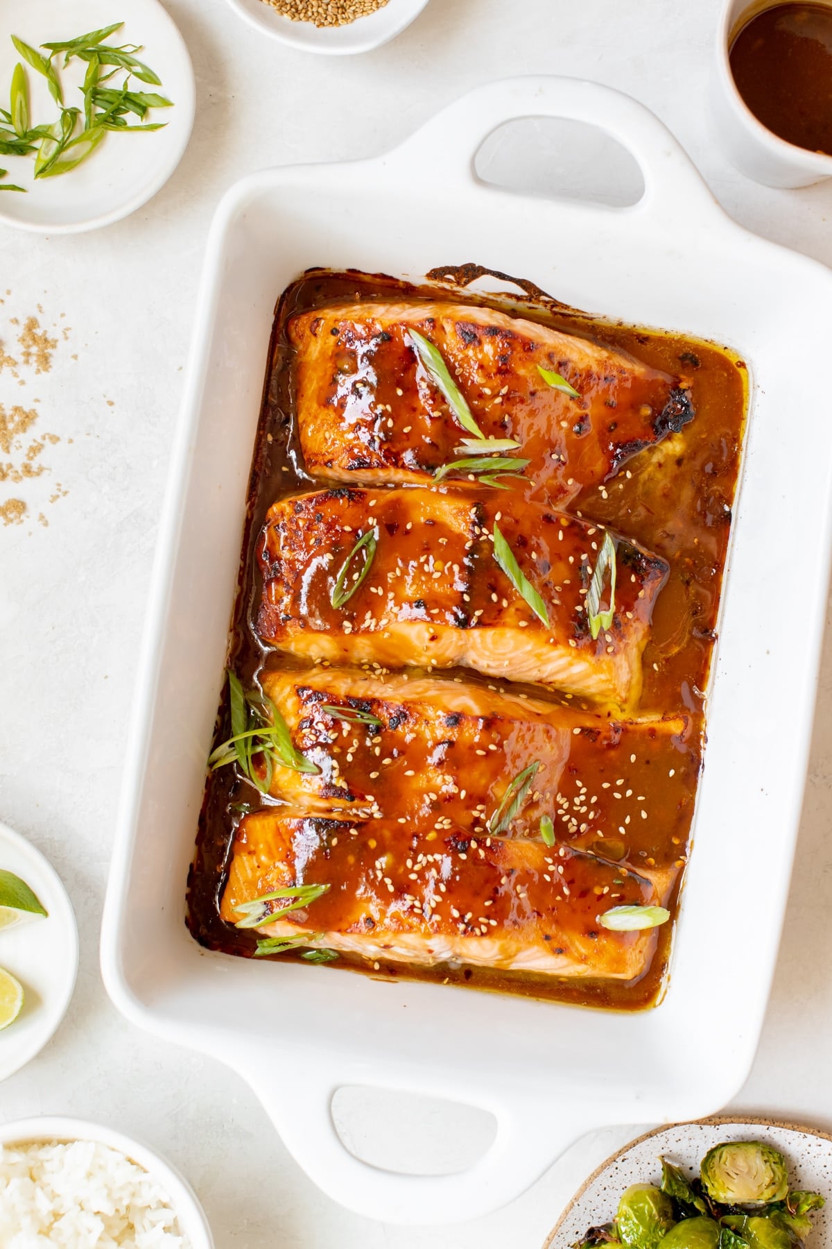 salmon in a white oven safe baking dish garnished with green onions and toasted sesame seeds