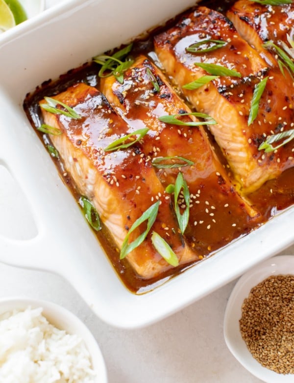 salmon in a white oven safe baking dish garnished with green onions and toasted sesame seeds