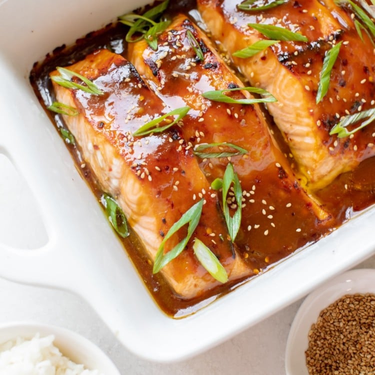 salmon in a white oven safe baking dish garnished with green onions and toasted sesame seeds