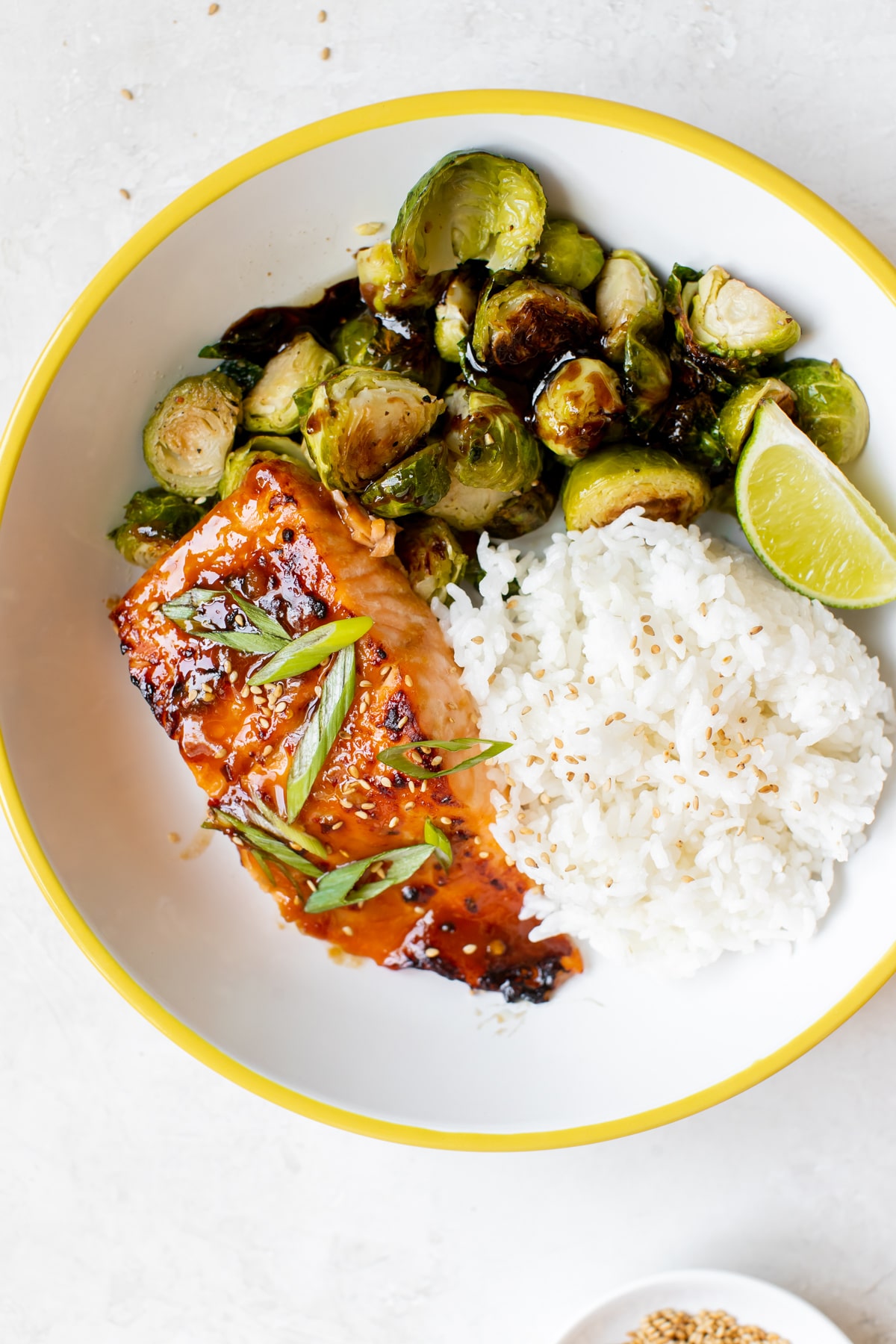 salmon, white rice and roasted brussels in a white bowl with yellow trim