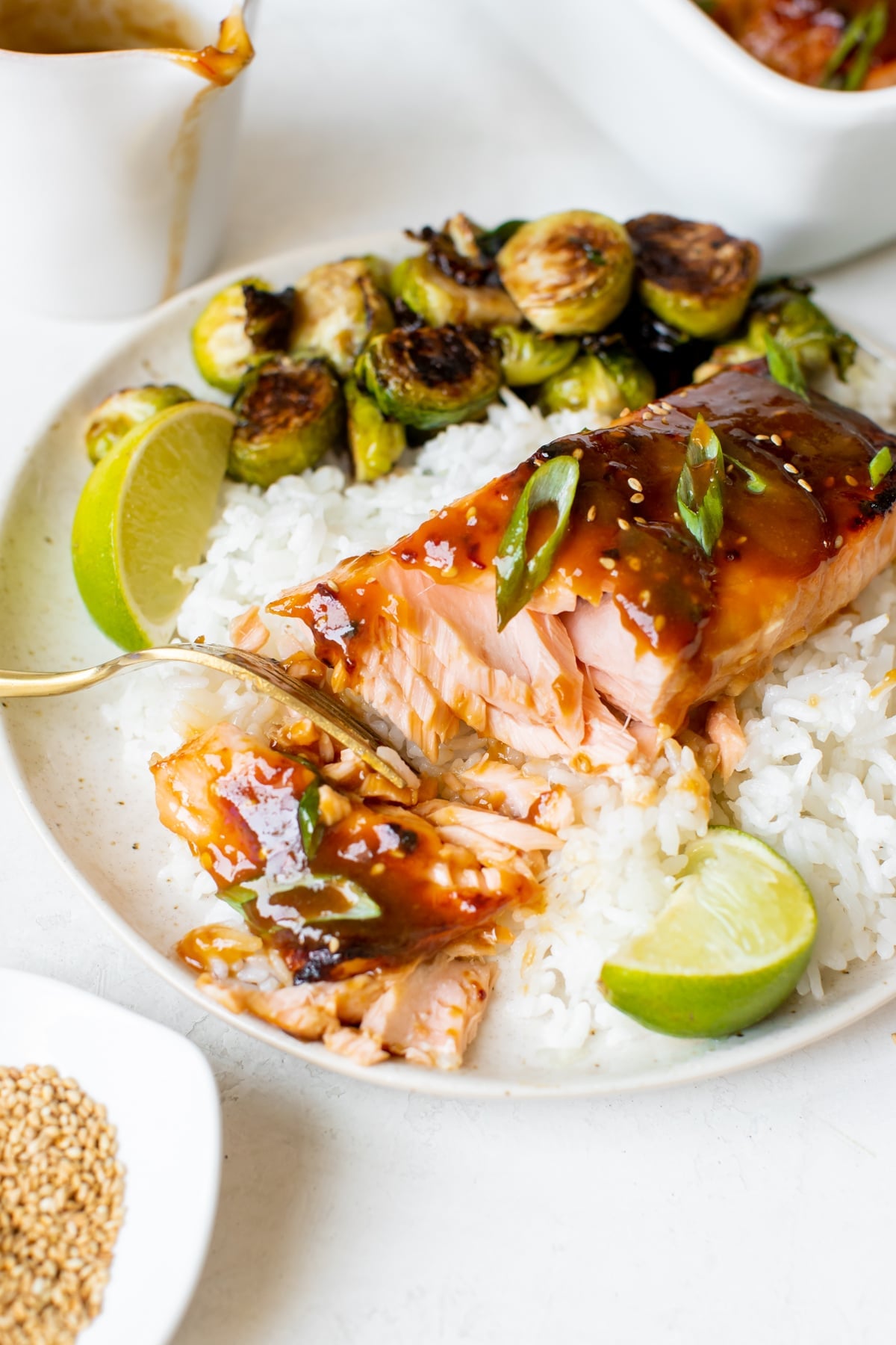 salmon with a gold fork flaking off a bite on a white plate with white rice and roasted brussels