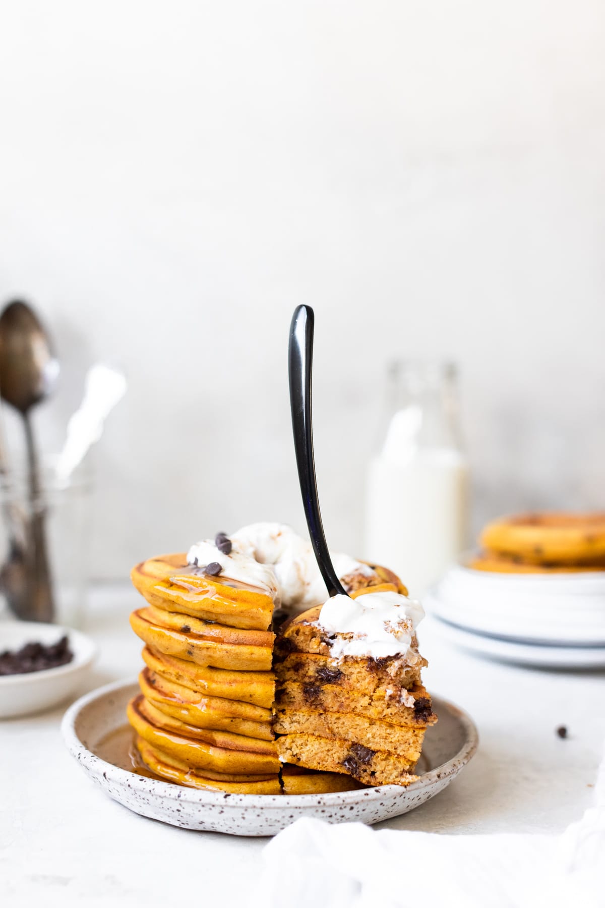 pancakes on a white speckled plate with a black fork in the pancakes