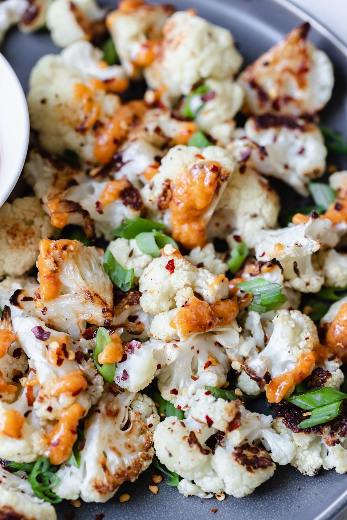 roasted cauliflower on a dark grey plate with miso sauce and green onions on top
