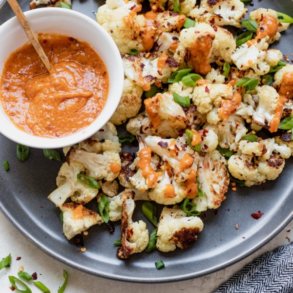 roasted cauliflower on a dark grey plate with miso sauce and green onions on top