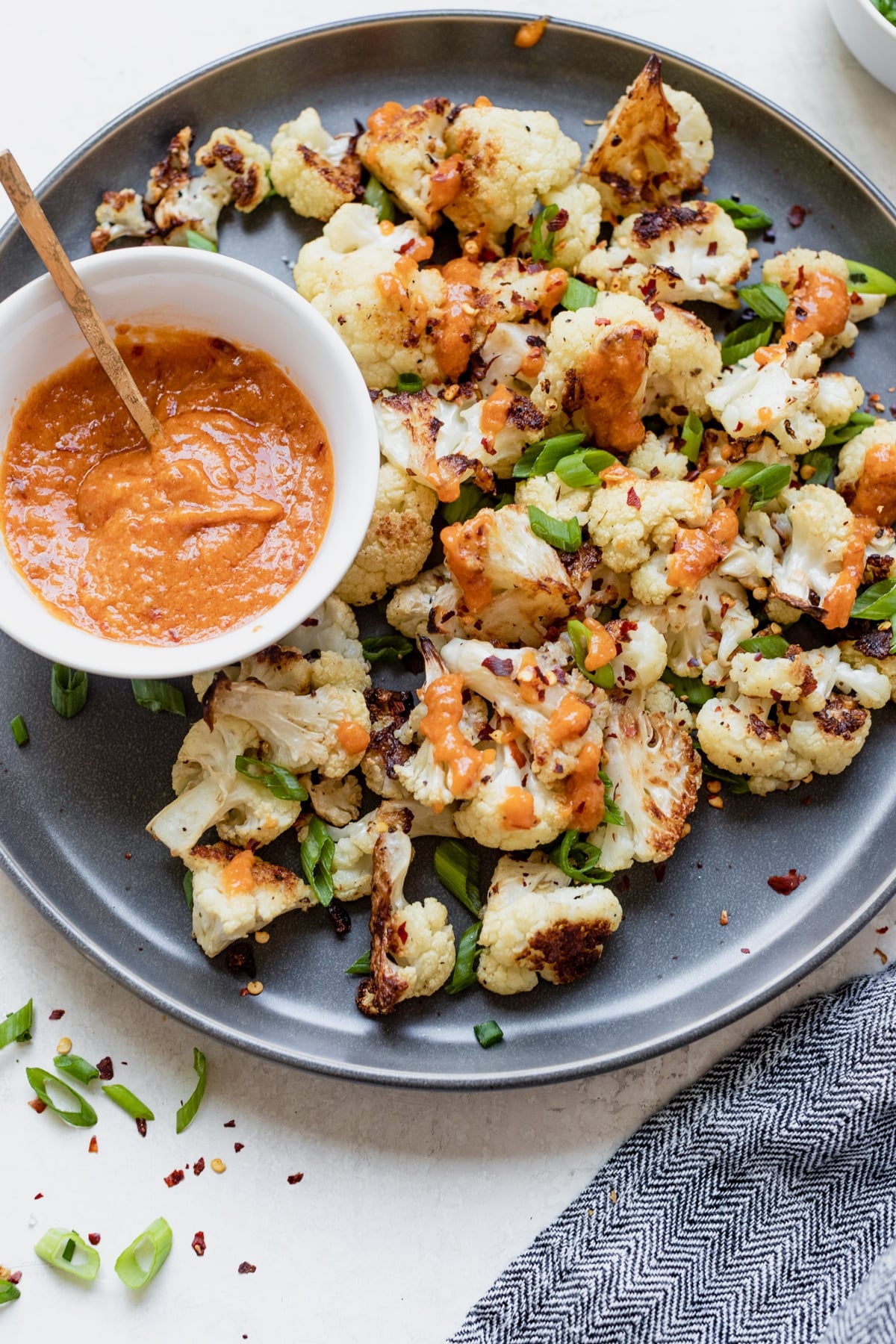 roasted cauliflower on a dark grey plate with miso sauce and green onions on top