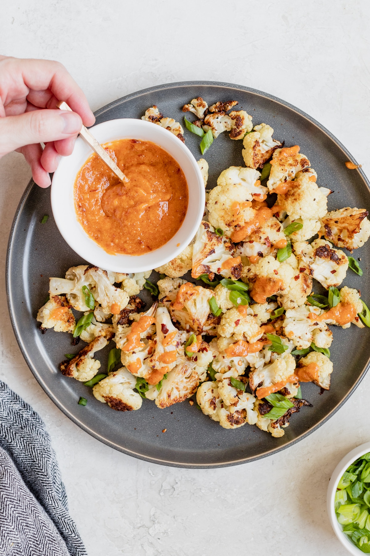 roasted cauliflower on a dark grey plate with miso sauce and green onions on top