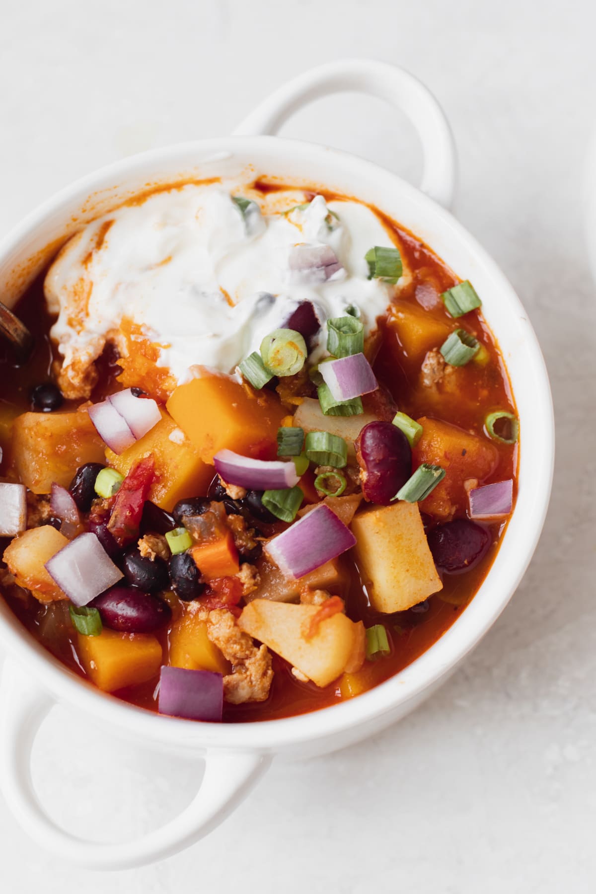 chili in a white soup bowl topped with green onions and sour cream