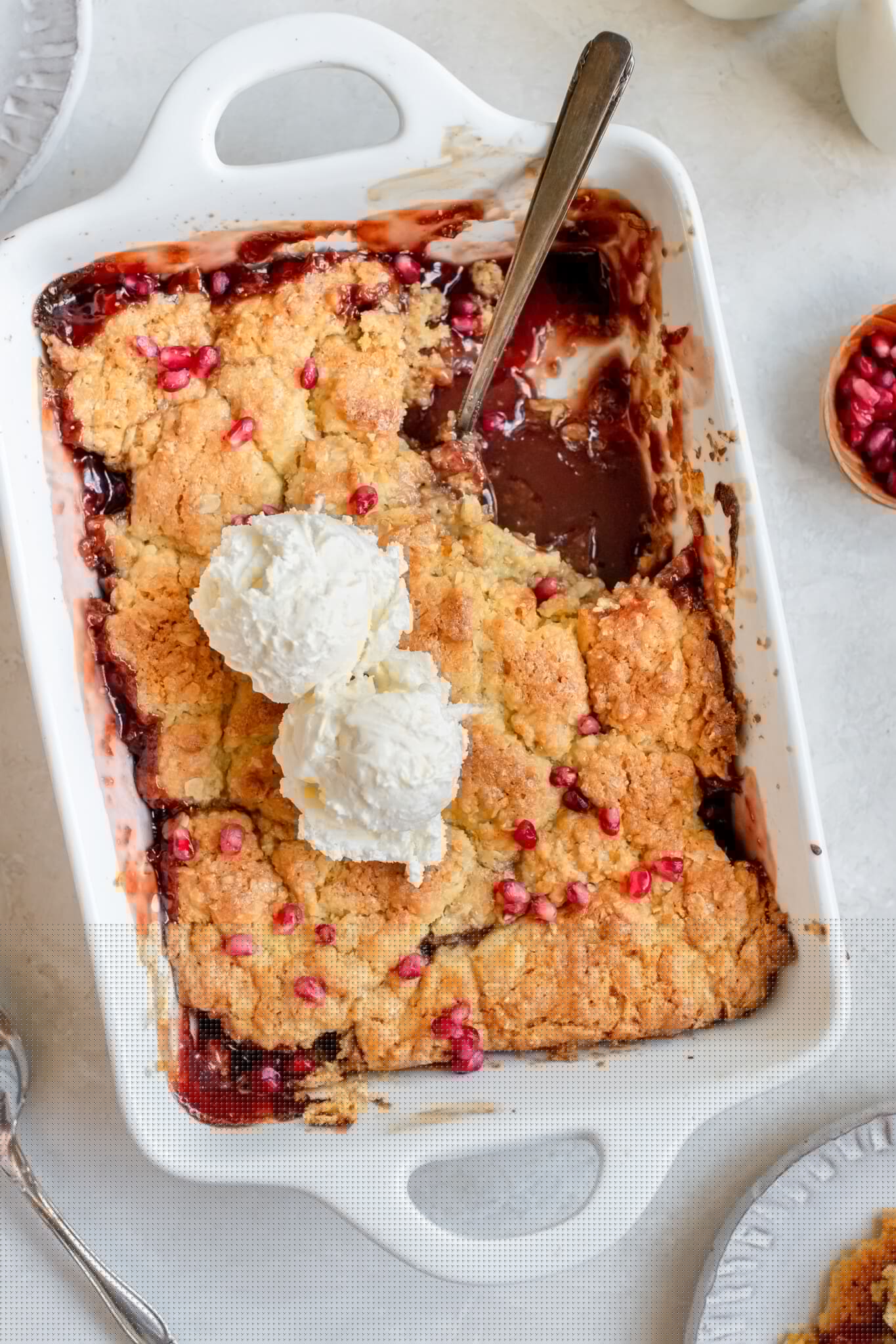 apple cobbler in a white baking dish topped with ice cream and pomegranate seeds