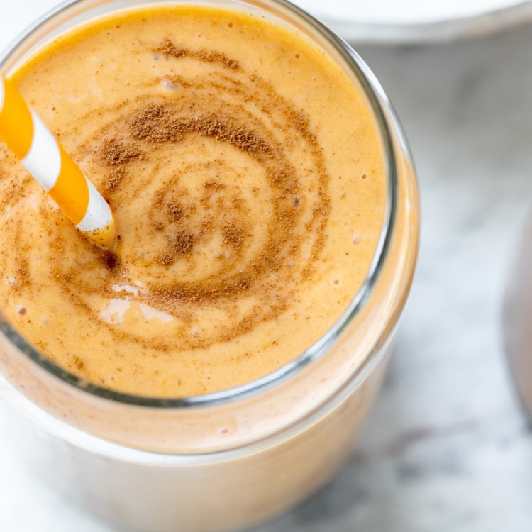 a smoothie made with pumpkin in a glass cup garnished with cinnamon and an orange straw