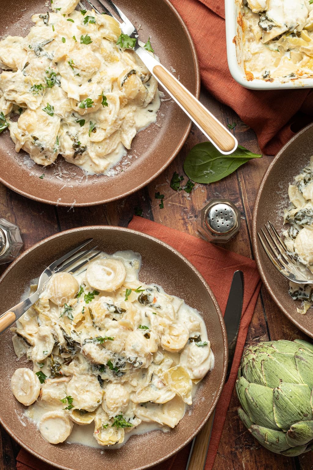 bowls of spinach artichoke pasta with fork