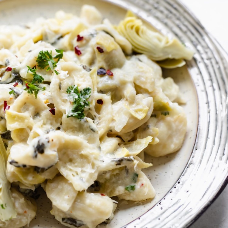 orecchiette pasta on a plate covered in cheese, spinach and artichokes