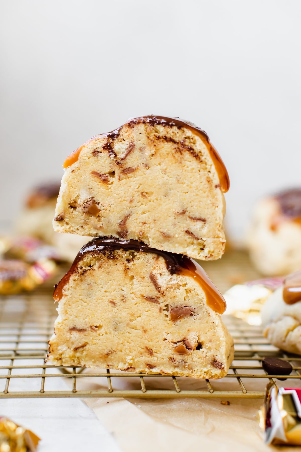 a giant cookie topped with chocolate, caramel and sea salt cut in half on a gold cooling rack