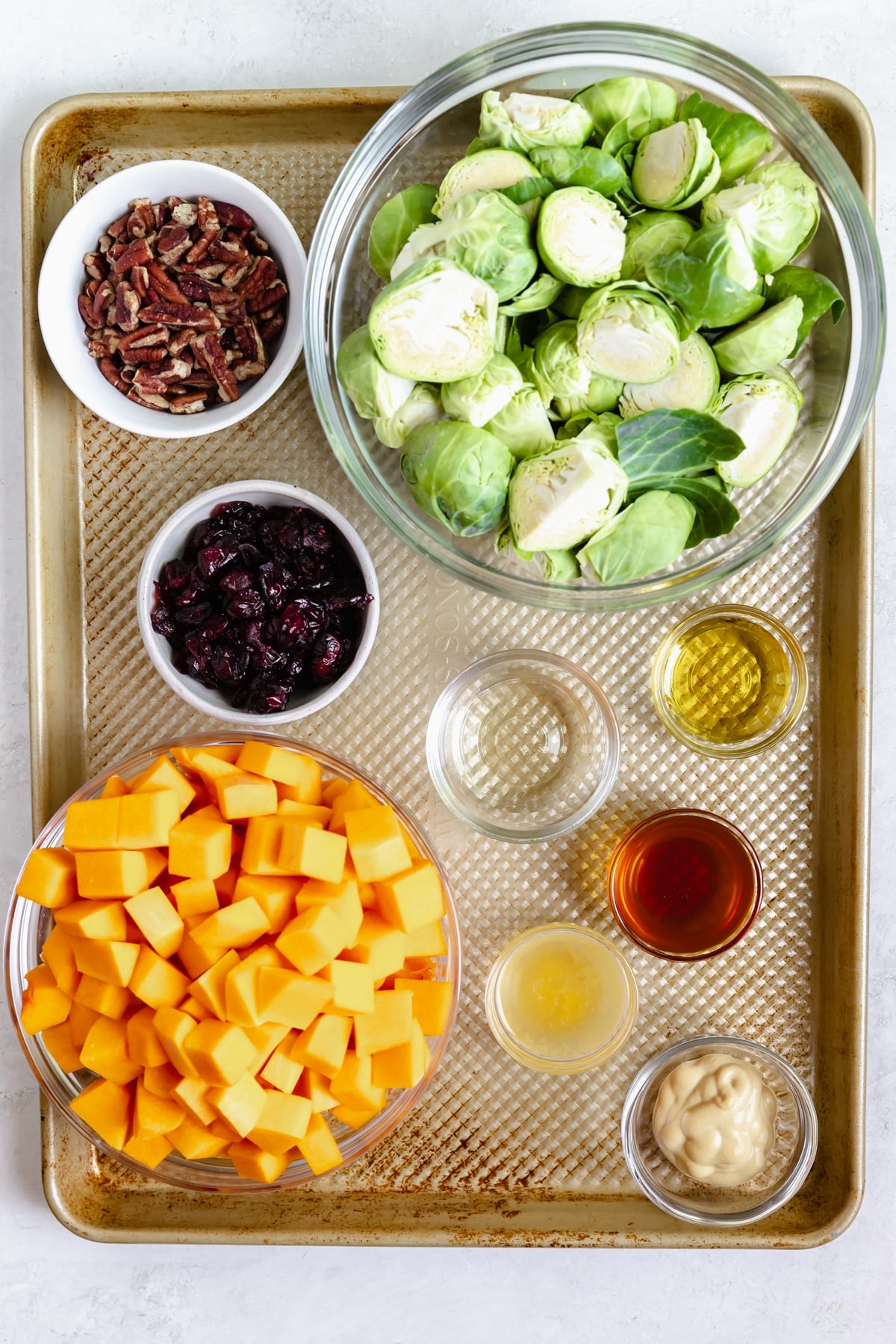 ingredients needed to make roasted brussels sprouts and butternut squash in small dishes on a gold sheet pan