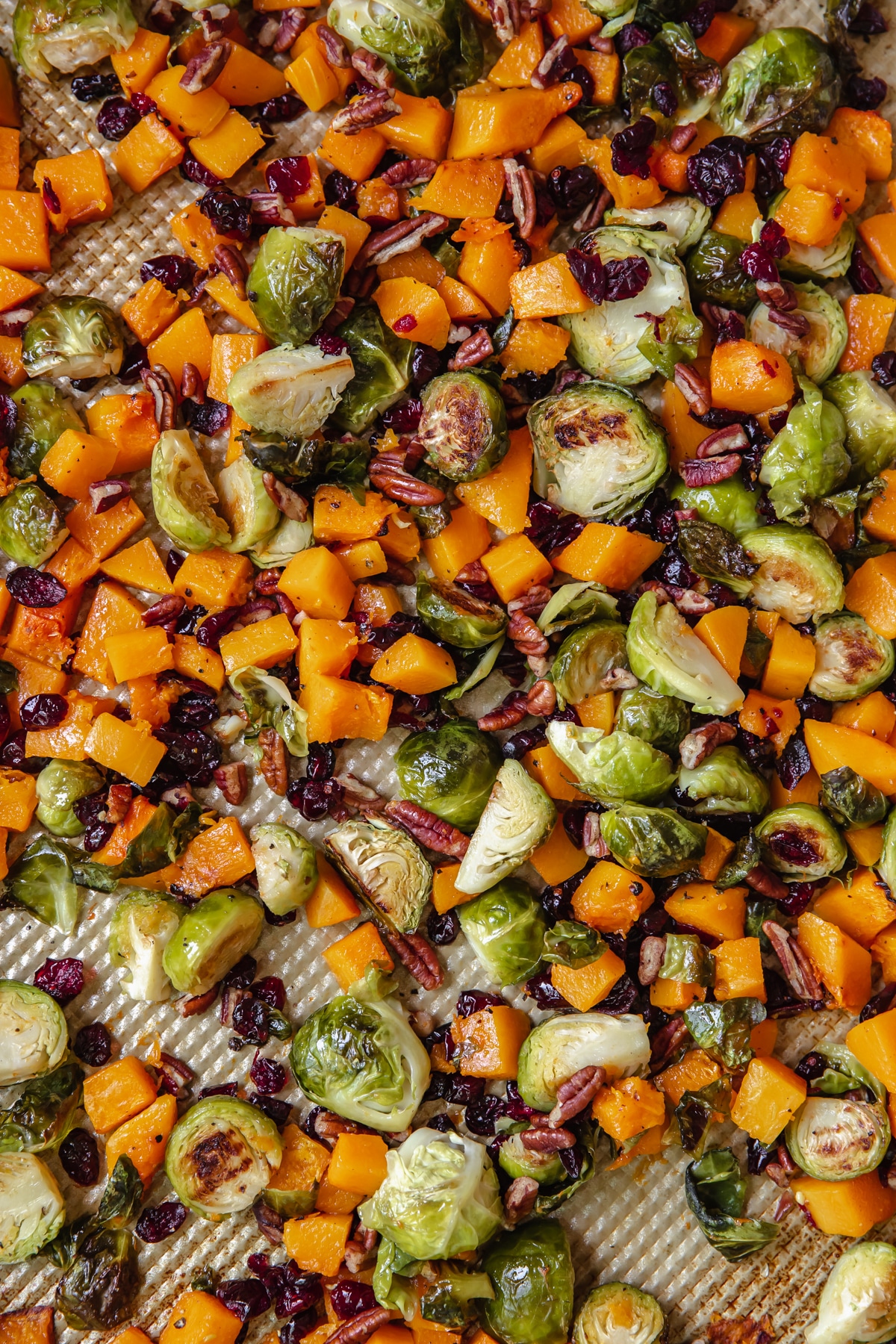 veggies on a gold sheet pan garnished with chopped pecans and dried cranberries